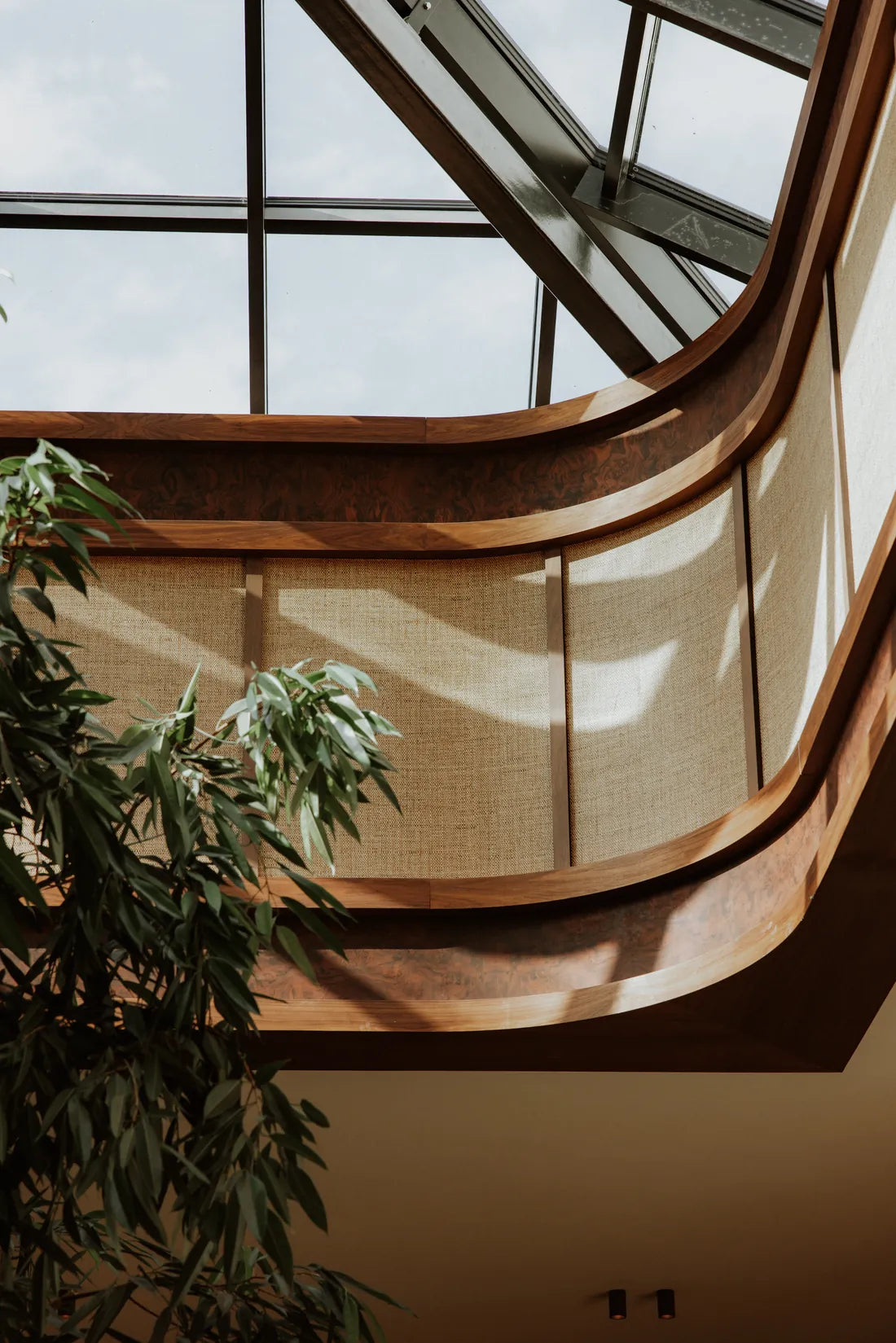 A curved timber balcony and indoor foliage beneath the glass atrium roof at CORI Hornbæk.