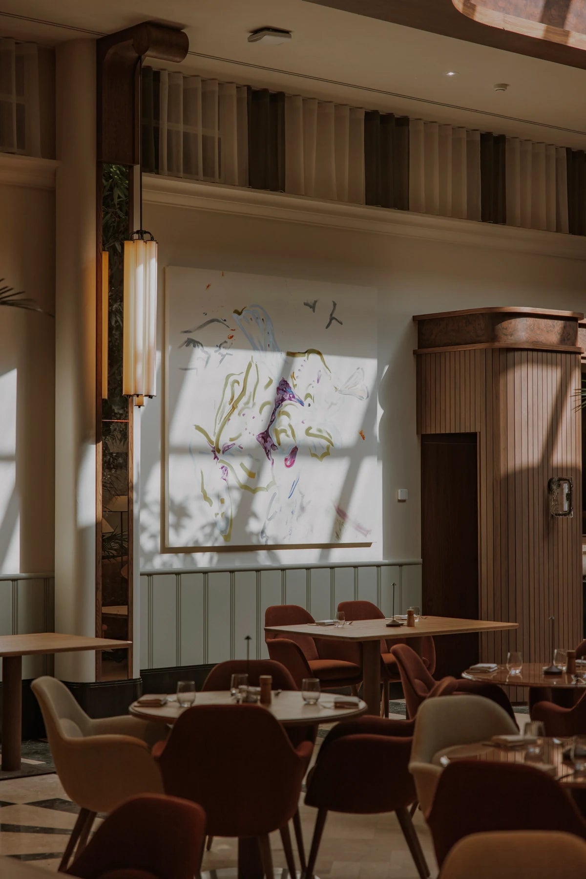 Sunlight falls across tables and upholstered chairs in a dining room at CORI Hornbæk.