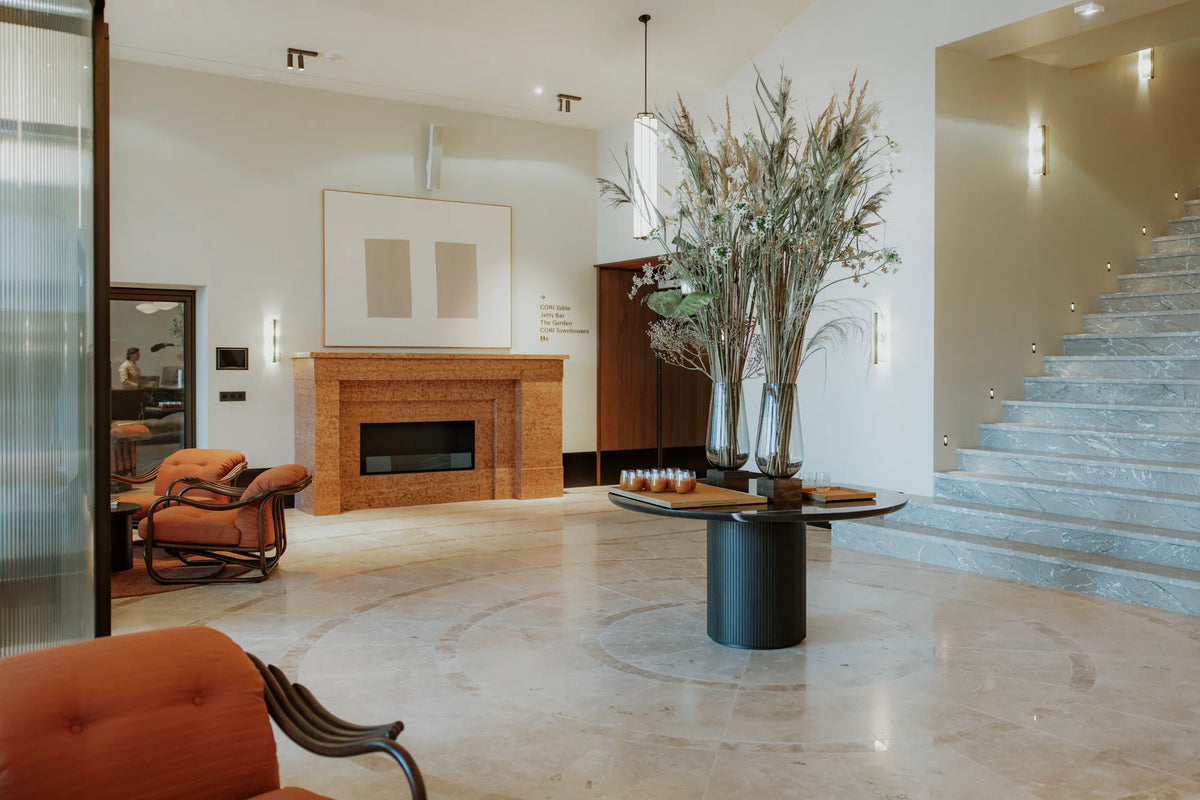 A bright lobby at CORI Hornbæk with a fireplace, floral arrangement and stone staircase.