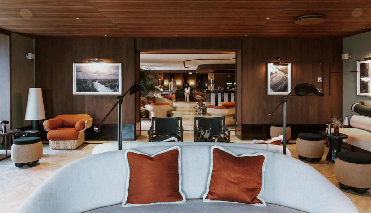 A curved pale sofa with rust-coloured cushions in the timber-lined lounge at CORI Hornbæk.