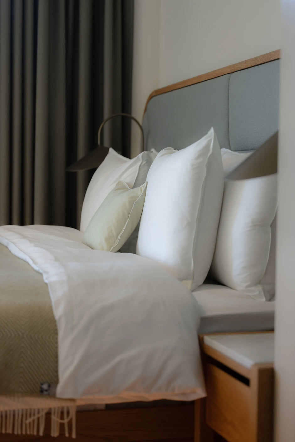 White pillows and bedding beside a timber bedside table at CORI Hornbæk.