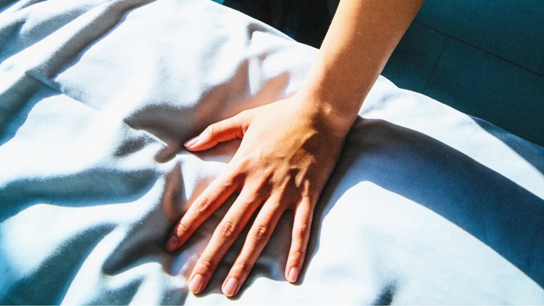 Person lying on a bed with a hand on their chest, standing person in the background.